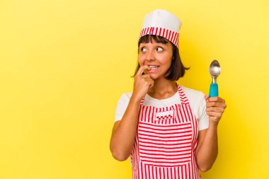 Genç melez dondurma üreticisi kadın sarı arka planda izole edilmiş bir dondurma tutuyor. Küçük melez dondurma üreticisi kadın sarı arka planda izole edilmiş dondurma kepçesini tutuyor. Bir şeyin fotokopi alanına baktığını düşünerek rahatlıyor..