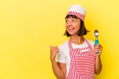 Genç melez dondurma üreticisi kadın sarı arka planda izole edilmiş bir dondurma tutuyor. Genç melez dondurma üreticisi kadın sarı arka planda izole edilmiş bir dondurma kepçesi tutuyor. Parmak uzakta, gülüyor ve kaygısız..