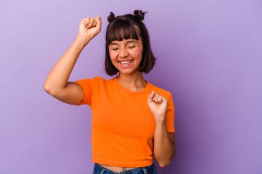 Mor arka planda izole edilmiş genç bir ırk kadını özel bir günü kutluyor, atlıyor ve enerji ile kollarını kaldırıyor..