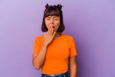 Mor arka planda izole edilmiş genç bir ırk kadını esniyor. Ağzıyla ağzını kapatan yorgun bir jest gösteriyor..