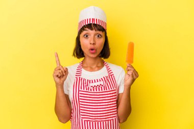 Genç melez dondurma üreticisi kadın dondurma tutuyor sarı arka planda izole edilmiş harika bir fikri var, yaratıcılık kavramı..