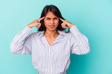 Mavi arka planda izole edilmiş genç Latin bir kadın bir göreve odaklanmış, işaret parmaklarını işaret ediyor..