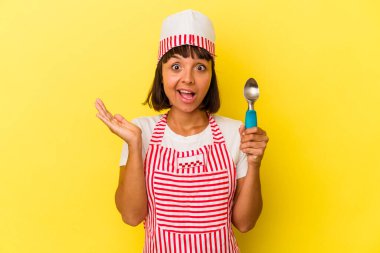 Genç melez dondurma üreticisi kadın, sarı arka planda izole edilmiş dondurma tutuyor. Küçük melez dondurma üreticisi kadın, sarı arka planda izole edilmiş dondurma kepçesini tutuyor. Şaşırmış ve şok olmuş..