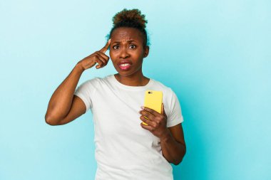 Mavi arka planda cep telefonu tutan genç Afrikalı Amerikalı kadın işaret parmağıyla yaptığı hayal kırıklığı jestini gösteriyor..