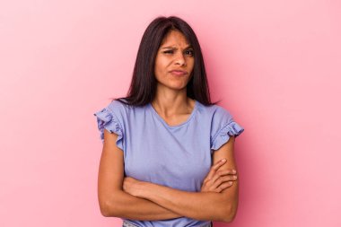 Pembe arka planda izole edilmiş, hoşnutsuzca kaşlarını çatan, kollarını kavuşturan genç Latin bir kadın..