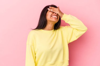 Pembe arka planda soyutlanmış genç Latin bir kadın elleriyle gözlerini kapatıyor, geniş bir gülümsemeyle bir sürpriz bekliyor..