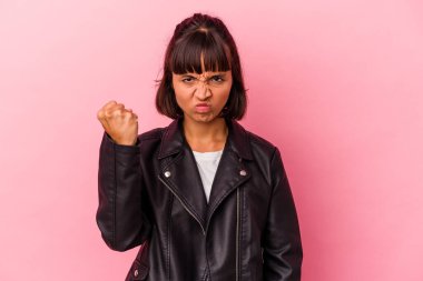 Pembe arka planda izole edilmiş genç bir ırk kadını kameraya yumruk gösteriyor, agresif bir yüz ifadesi..