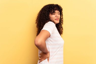 Sarı arka planda izole edilmiş, sırt ağrısı çeken genç bir ırk kadını..