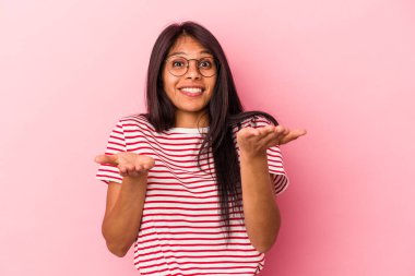 Pembe arka planda izole edilmiş genç Latin kadın kollarıyla ölçek oluşturuyor, mutlu ve kendinden emin hissediyor..