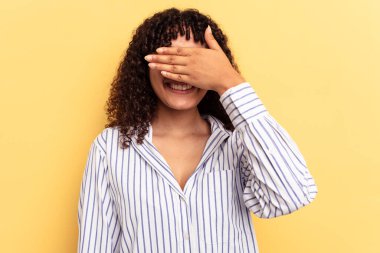 Sarı arka planda soyutlanmış genç bir ırk kadını. Gözleri ellerle kaplıyor. Gülümsüyor ve bir sürpriz bekliyor..