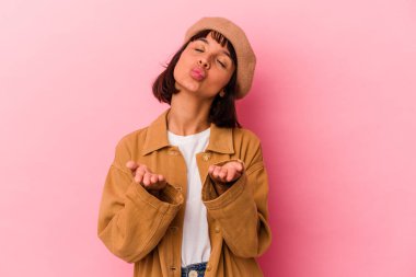 Genç melez kadın pembe arka planda izole edilmiş dudaklar kıvrılmış ve hava öpücüğü göndermek için avuç içleri tutulmuş..