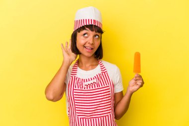 Genç melez dondurma üreticisi kadın dondurma tutuyor sarı arka planda izole edilmiş bir şekilde bir dedikoduyu dinliyor..