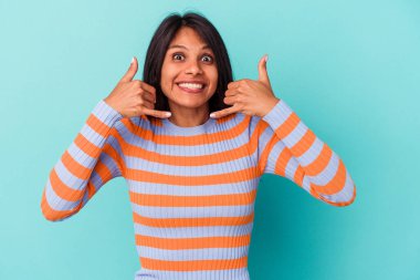 Mavi arka planda izole edilmiş genç Latin kadın parmakları olan bir cep telefonu hareketi gösteriyor..