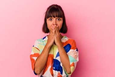 Pembe arka planda izole edilmiş genç melez kadın elleri endişeli bir şekilde ağzı örtüyor..