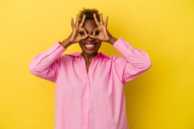 Sarı arka planda izole edilmiş genç Afrikalı Amerikalı kadın gözlerinde iyi işareti gösteriyor.