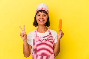 Genç melez dondurma üreticisi kadın, sarı arka planda izole edilmiş dondurma tutuyor neşeli ve tasasız parmakları olan bir barış sembolü gösteriyor..