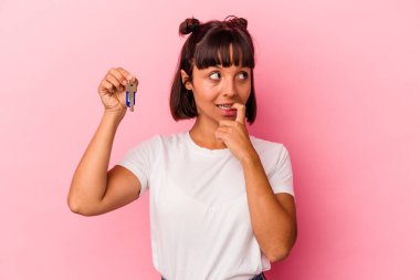 Pembe arka planda izole edilmiş bir anahtar tutan genç bir ırk kadını rahat bir şekilde fotokopi odasına bakan bir şeyi düşünüyor..