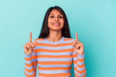 Mavi arka planda izole edilmiş genç Latin bir kadın iki ön parmağı da boş bir alan gösteriyor..