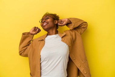 Genç Afrikalı Amerikalı kadın, sarı arka planda izole edilmiş, kollarını açmış, rahat bir pozisyonda..