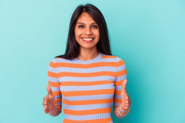 Mavi arka planda izole edilmiş genç Latin kadın iki eliyle bir şey tutuyor, ürün sunumu..