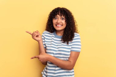Sarı arka planda izole edilmiş genç melez kadın işaret parmağıyla fotokopi alanını işaret ederek şok oldu..