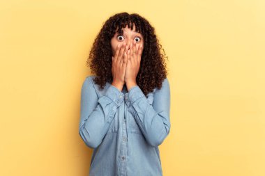 Sarı arka planda izole edilmiş genç bir ırk kadını elleriyle ağzını kapatırken şok oldu..
