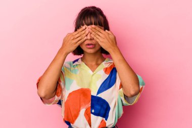 Pembe arka planda soyutlanmış genç melez kadın elleriyle gözlerini kapatmaktan korkuyor..