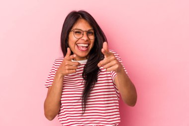 Pembe arka planda soyutlanmış genç Latin bir kadın. Neşeli gülümsemeler öne bakıyor..