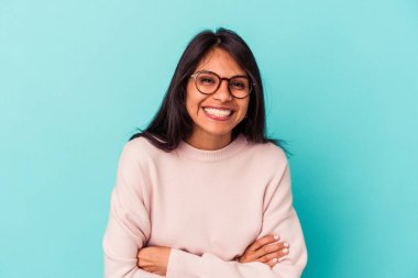 Mavi arka planda yalnız yaşayan genç Latin kadın gülüyor ve eğleniyor..