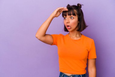 Mor arka planda izole edilmiş genç bir ırk kadını uzaklara bakıyor ve elini alnına koyuyor..