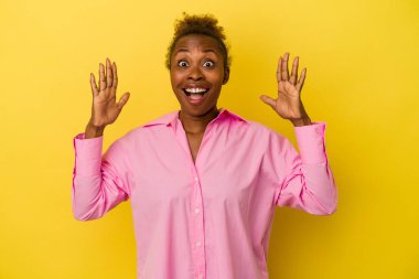 Sarı arka planda izole edilmiş genç Afro-Amerikalı kadın zaferi ya da başarıyı kutluyor, şaşırıyor ve şok oluyor..