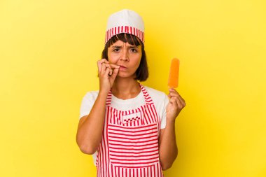 Dondurma üreten genç bir kadın sarı arka planda izole edilmiş dondurma tutuyor ve parmakları dudaklarında bir sır saklıyor..