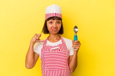 Sarı zemin üzerinde izole edilmiş dondurma tutan genç, melez bir dondurma üreticisi kadın. Sarı arka planda izole edilmiş dondurma kepçesini tutan genç, kendinden emin ve gururlu bir kadın..