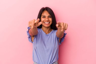 Pembe arka planda soyutlanmış genç Latin bir kadın. Neşeli gülümsemeler öne bakıyor..