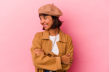 Pembe arka planda soyutlanmış genç melez bir kadın kollarını kavuşturarak gülümsüyor..