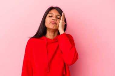 Pembe arka planda izole edilmiş genç Latin kadın yorgun ve uykulu ellerini başının üstünde tutuyor..