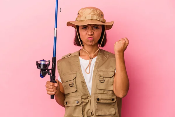 年轻的混血渔民女人拿着一根用粉色背景隔离的棒子 对着镜头 脸上充满攻击性的表情 — 图库照片