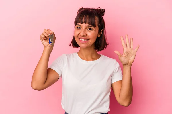 年轻的混血女子拿着一把用粉色背景隔开的钥匙 高兴地微笑着 用手指展示着第五名 — 图库照片