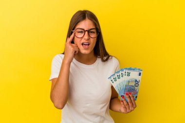 Elinde sarı arka planda izole edilmiş banknotlar tutan beyaz bir kadın işaret parmağıyla hayal kırıklığına uğradığını gösteriyor..