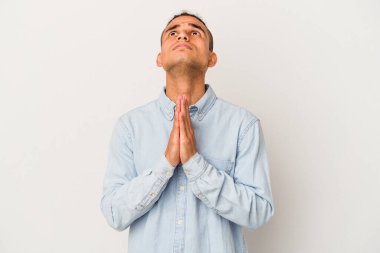 Genç Venezuellalı bir adam beyaz arka planda izole edilmiş, el ele tutuşmuş, ağız kenarında dua ediyor, kendinden emin..
