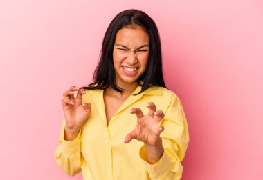 Genç Venezuelalı kadın pembe arka planda izole edilmiş pençelerini kedi taklidi yaparken gösteriyor, agresif bir hareket..