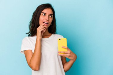 Mavi arka planda izole edilmiş cep telefonu tutan beyaz bir kadın. Bir şeyin fotokopi alanına baktığını düşünerek rahatlamış..