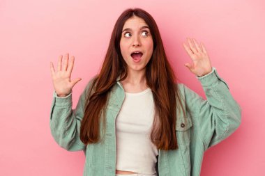 Pembe arka planda izole edilmiş genç beyaz kadın gökyüzüne haykırıyor, yukarı bakıyor, hayal kırıklığına uğramış..