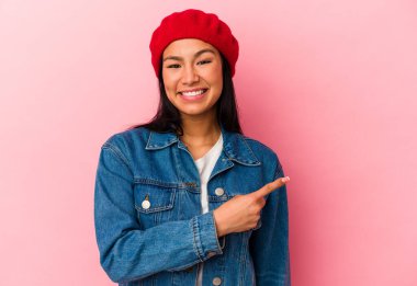 Genç Venezuelalı kadın pembe arka planda izole edilmiş gülümseyen ve işaret eden boş uzayda bir şey gösteriyor..