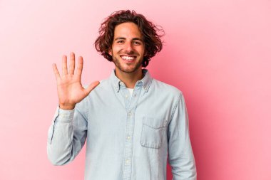 Pembe fırında izole edilmiş genç beyaz adam gülümseyerek beş numarayı parmaklarıyla gösteriyor..