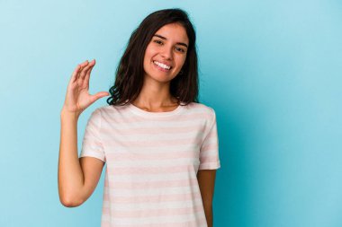 Kafkasyalı genç bir kadın mavi arka planda izole edilmiş. Elinde parmakları olan, gülümseyen ve kendinden emin bir şey var..