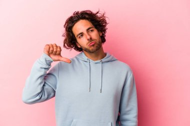 Pembe fırında izole edilmiş genç beyaz bir adam hoş olmayan bir jest yapıyor, başparmakları aşağıda. Anlaşmazlık konsepti.