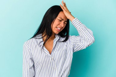 Genç Venezuelalı bir kadın mavi arka planda izole edilmiş bir şekilde bir şeyi unutuyor. Alnına avuç içi ve kapalı gözlerle vuruyor..