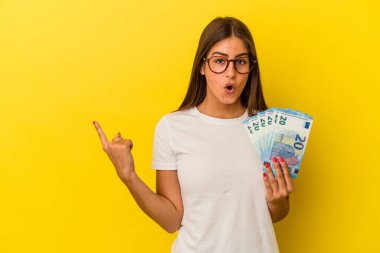 Elinde banknotlar tutan beyaz bir kadın. Sarı arka planda izole edilmiş. Yan tarafı işaret ediyor.