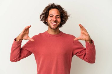 Beyaz arka planda izole edilmiş genç beyaz bir adam elinde avuç içi bir şeyle kameraya sunuyor..